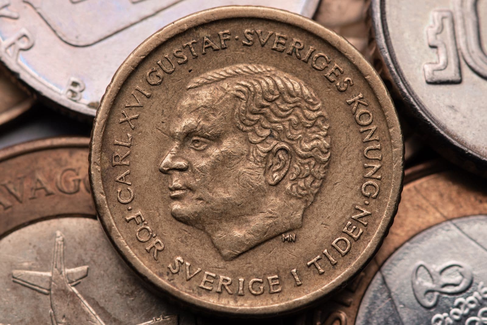 Close-up of a gold-coloured Swedish coin bearing the profile of King Carl XVI Gustaf, lying on a pile of other Swedish coins.
